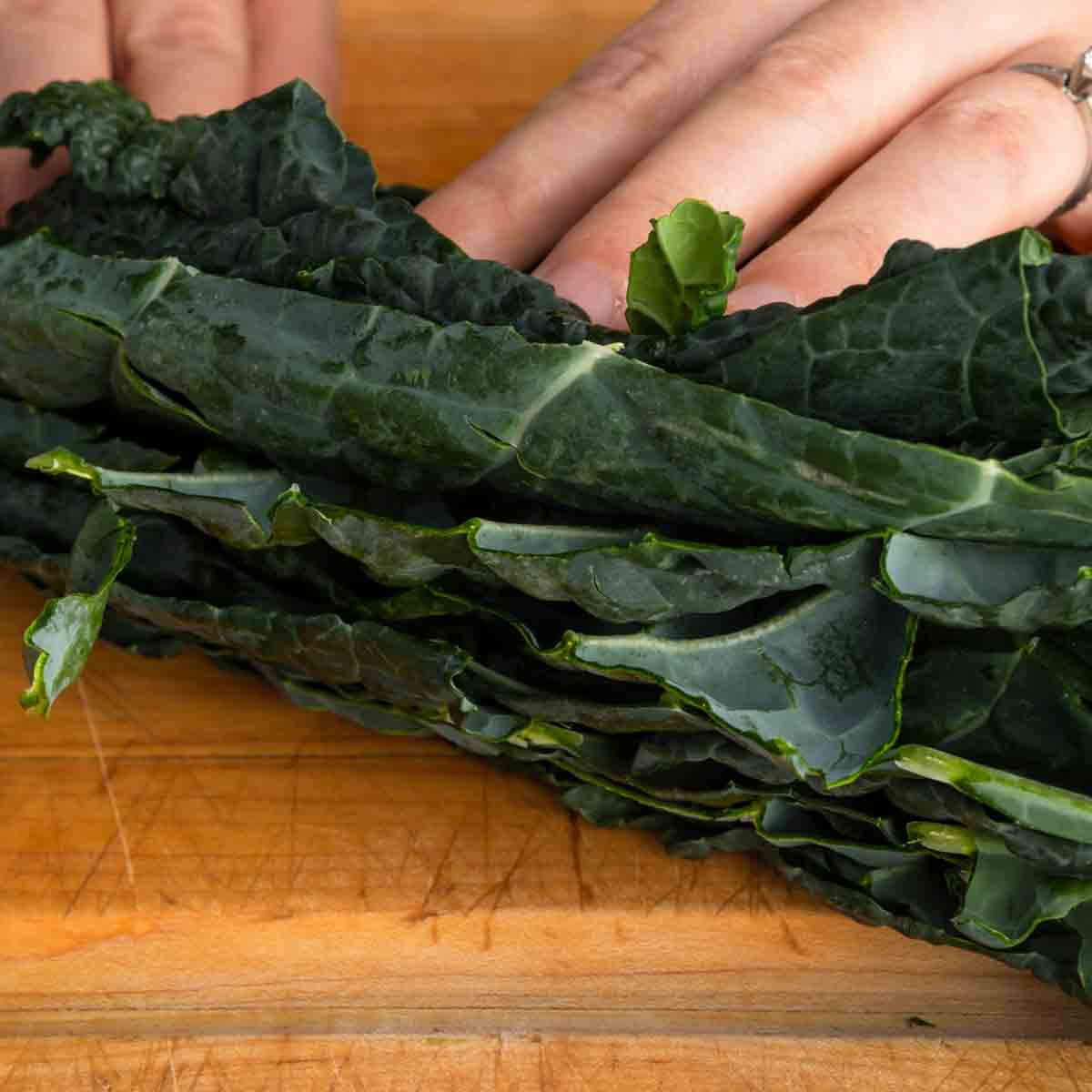 Stacking the kale leaves on top of each other on a cutting board.