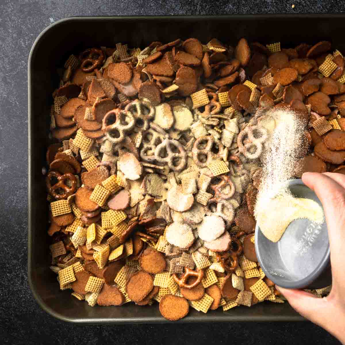 Sprinkling dry seasonings over the pan of buttered Chex mix.