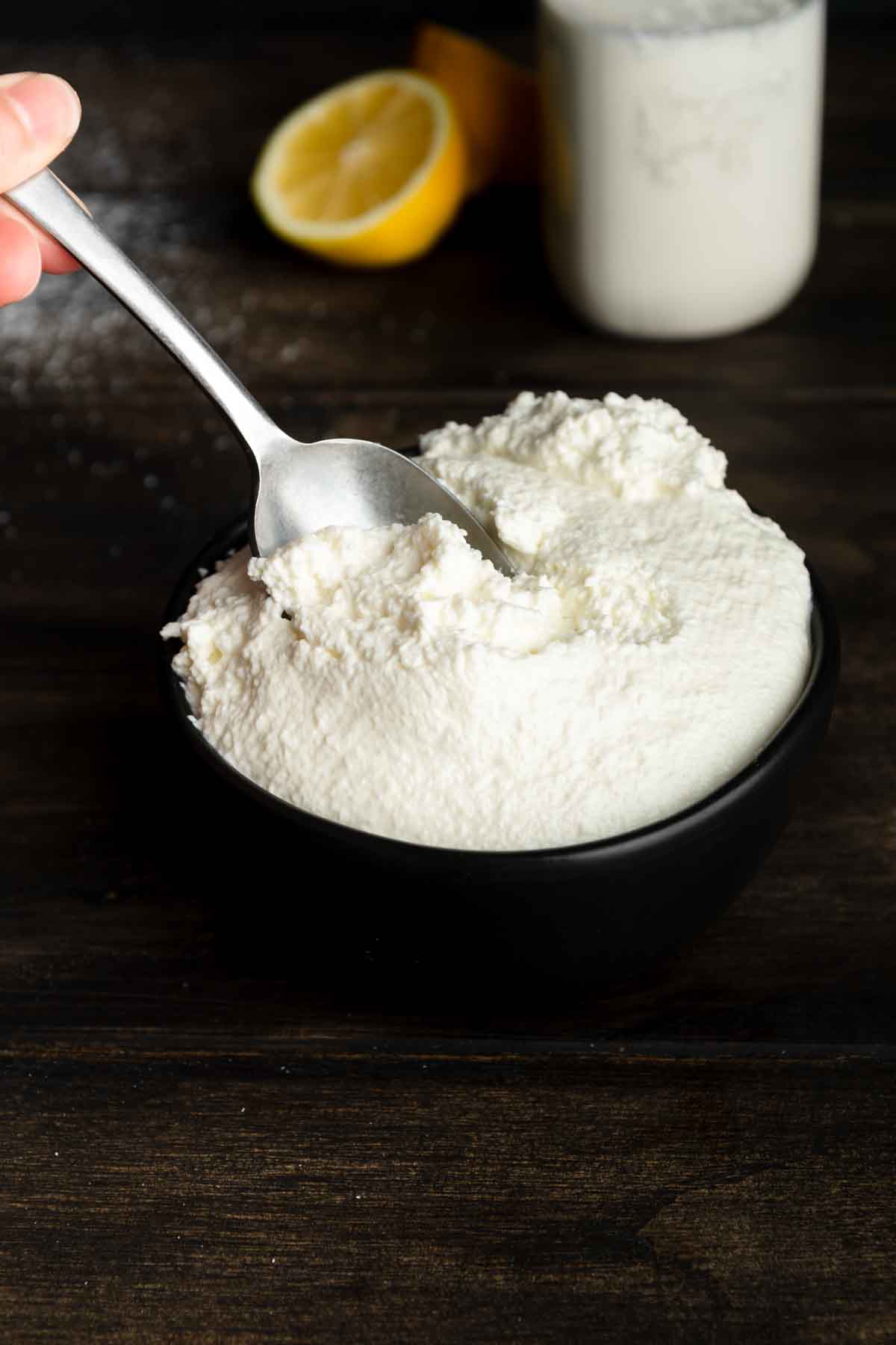 A spoon in a bowl filled with homemade ricotta cheese.