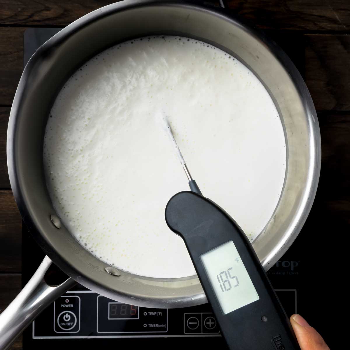 A pot of heated milk, cream and salt with an instant read thermometer reading 185° Fahrenheit.