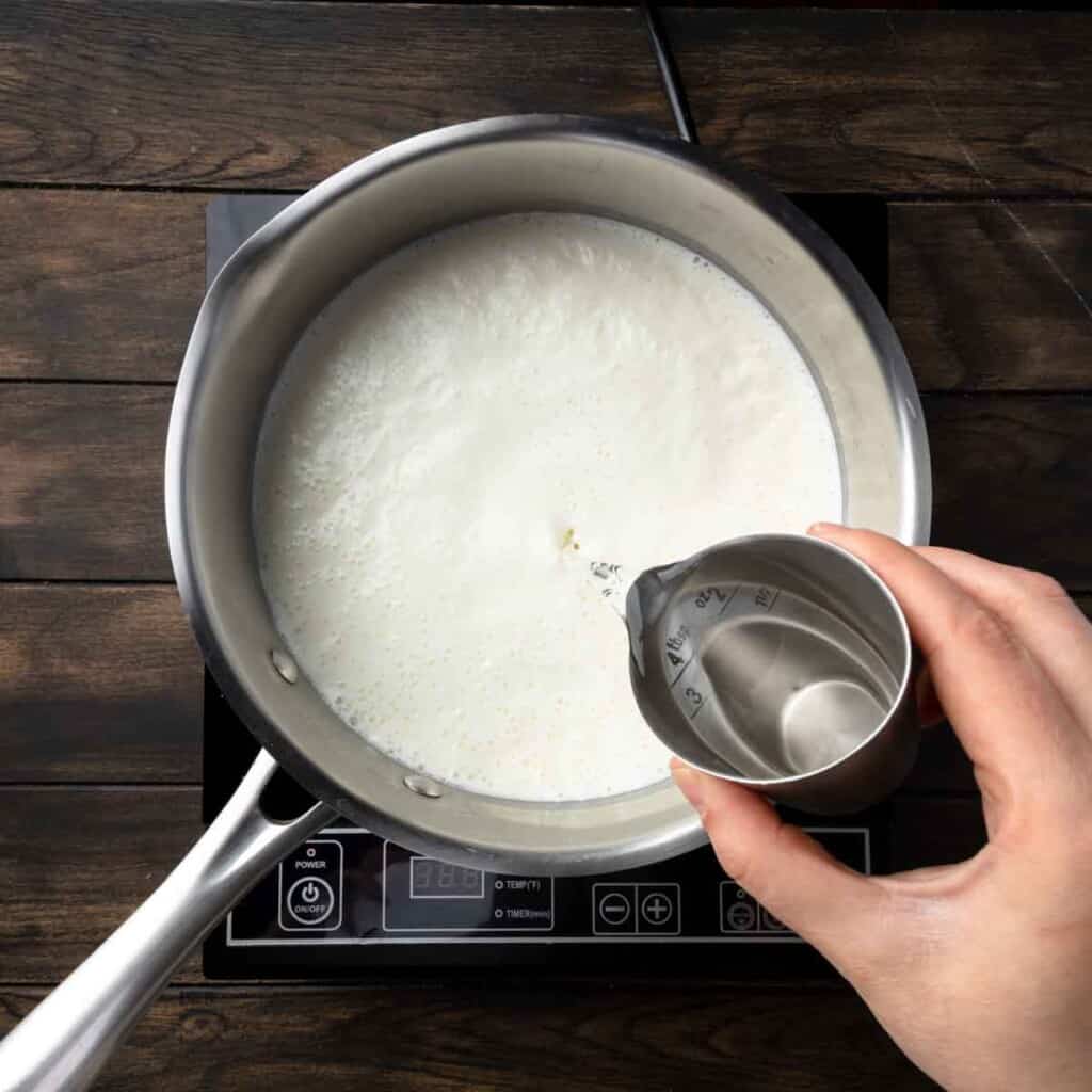 Pouring white vinegar into the pot of heated milk, cream and salt.