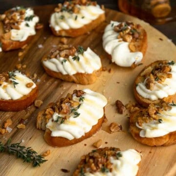 A wooden board with whipped ricotta crostini with honey, thyme and walnuts.