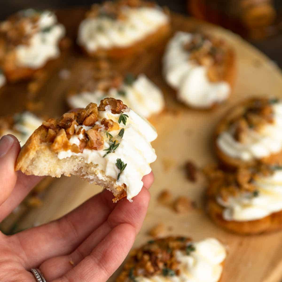 A hand holding a bitten ricotta crostini.