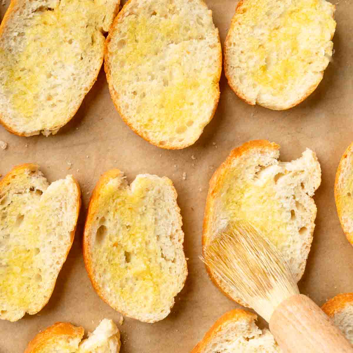 Brushing rounds of sliced baguette with olive oil.