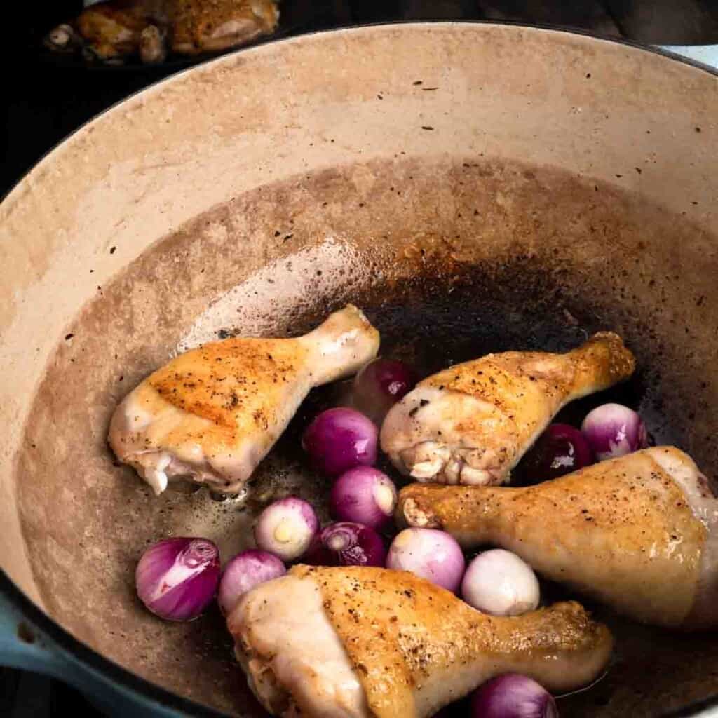 Seared chicken legs in a Dutch oven with pearl onions.