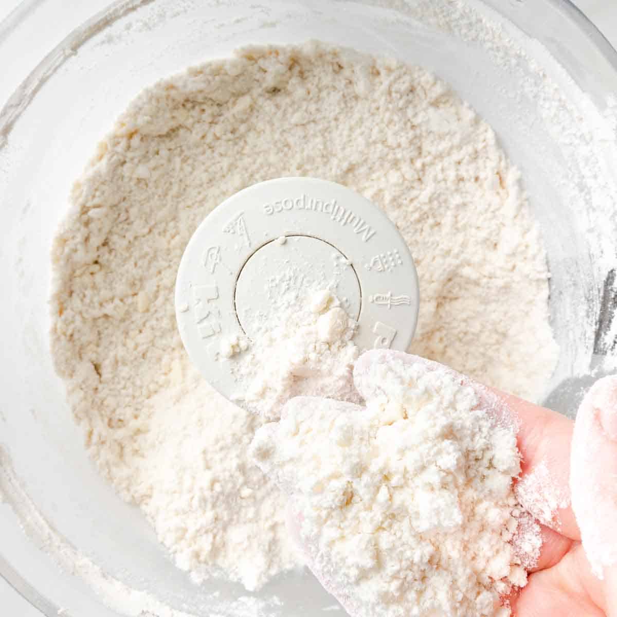 A hand holding up some of the sandy textured dough mixture.