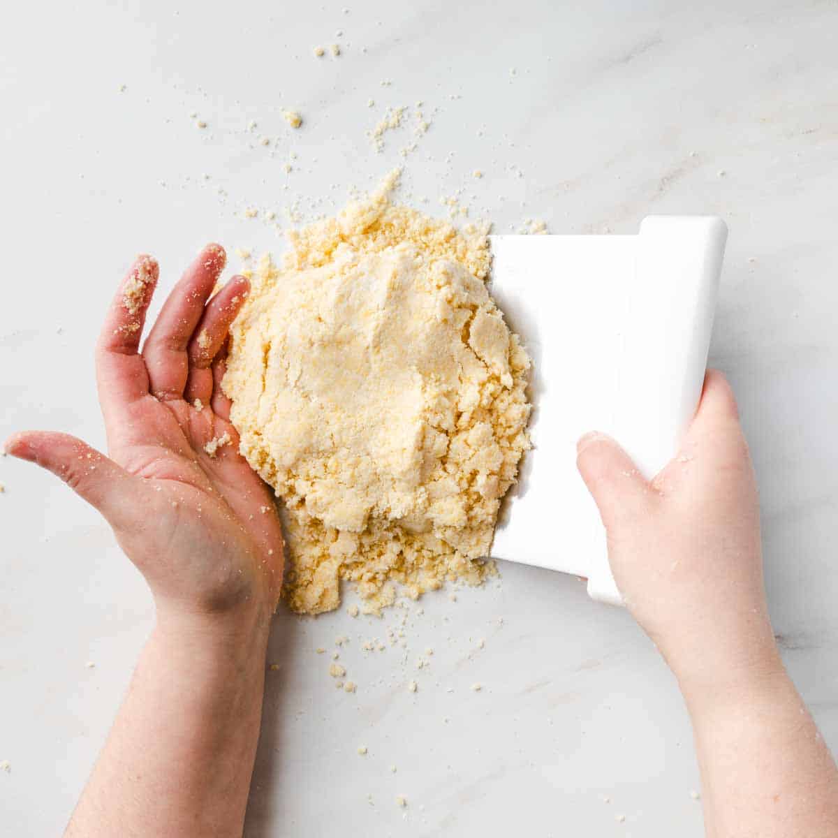 Using hands and a bench scraper to pull the crumbly pasta frolla dough together.