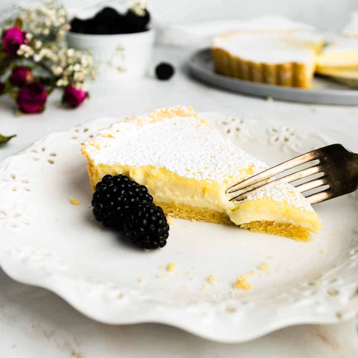 A fork taking the first bite off a slice of ricotta pie on a plate with blackberries.