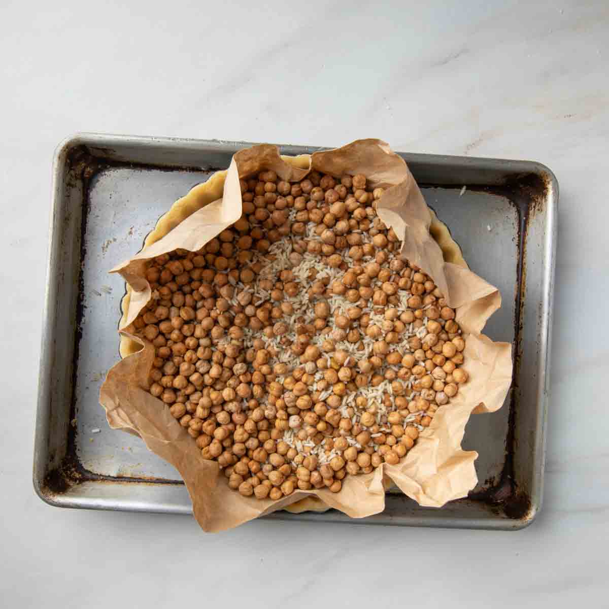 A pie crust lined with parchment and filled with rice and beans.