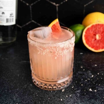 A pink mezcal Paloma cocktail garnished with smoked salt and fresh grapefruit.