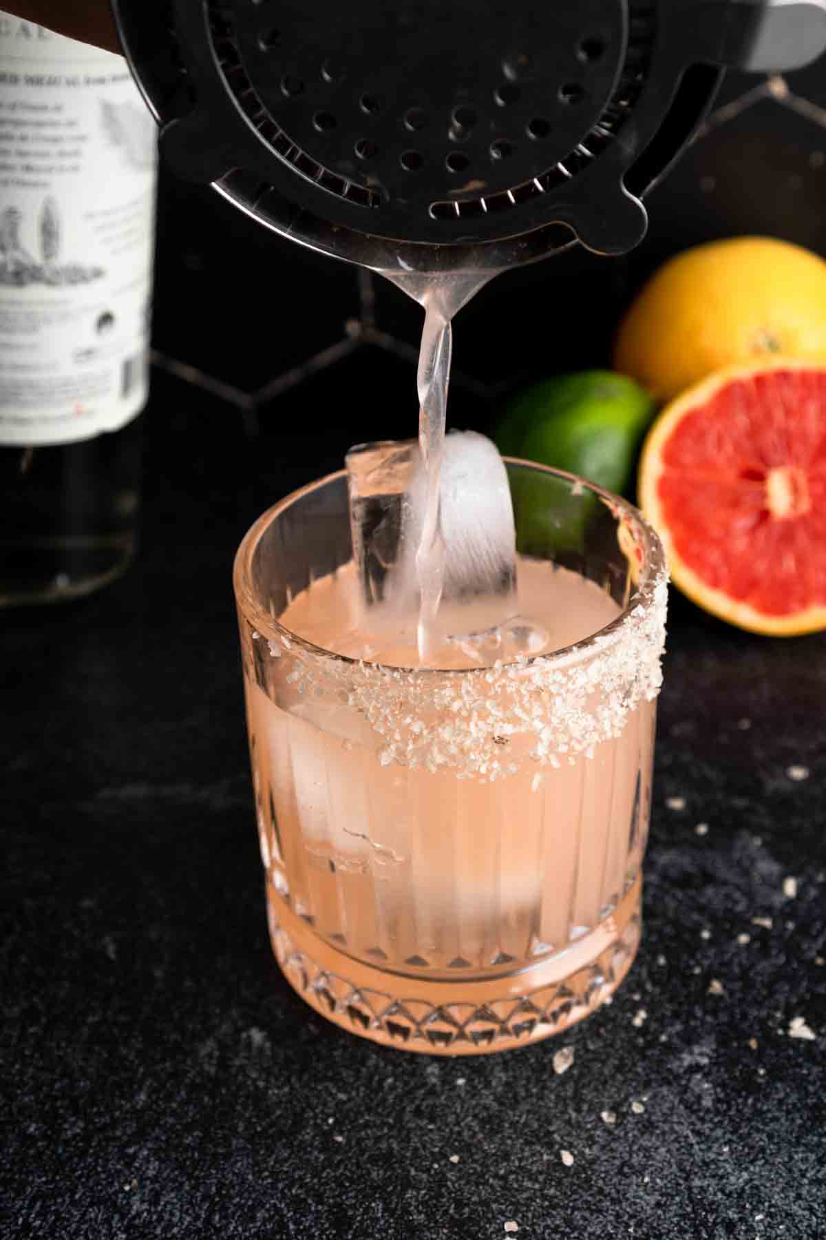 Pouring a mezcal grapefruit cocktail into a glass over ice.