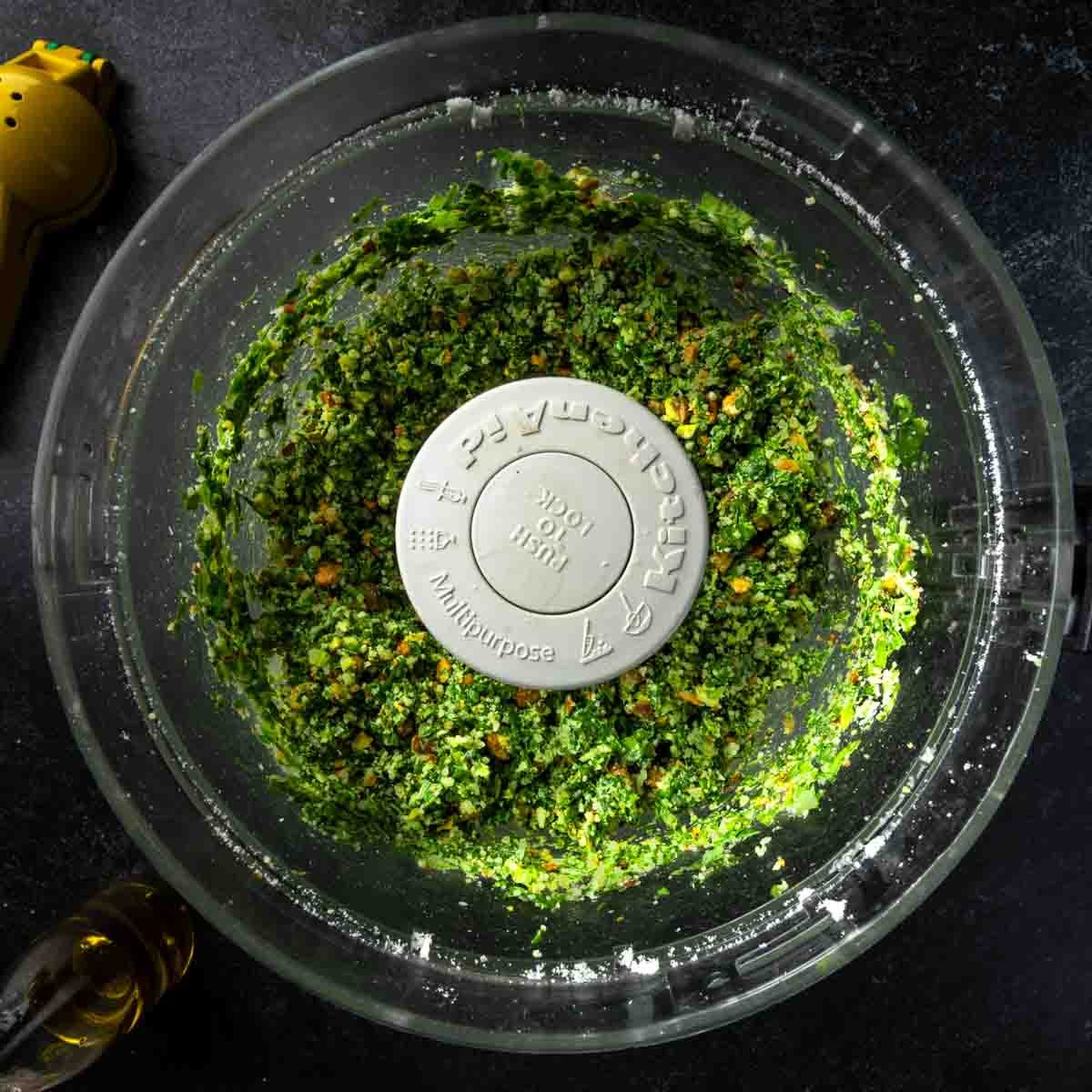 Coarsely processed spinach pesto ingredients in a food processor.