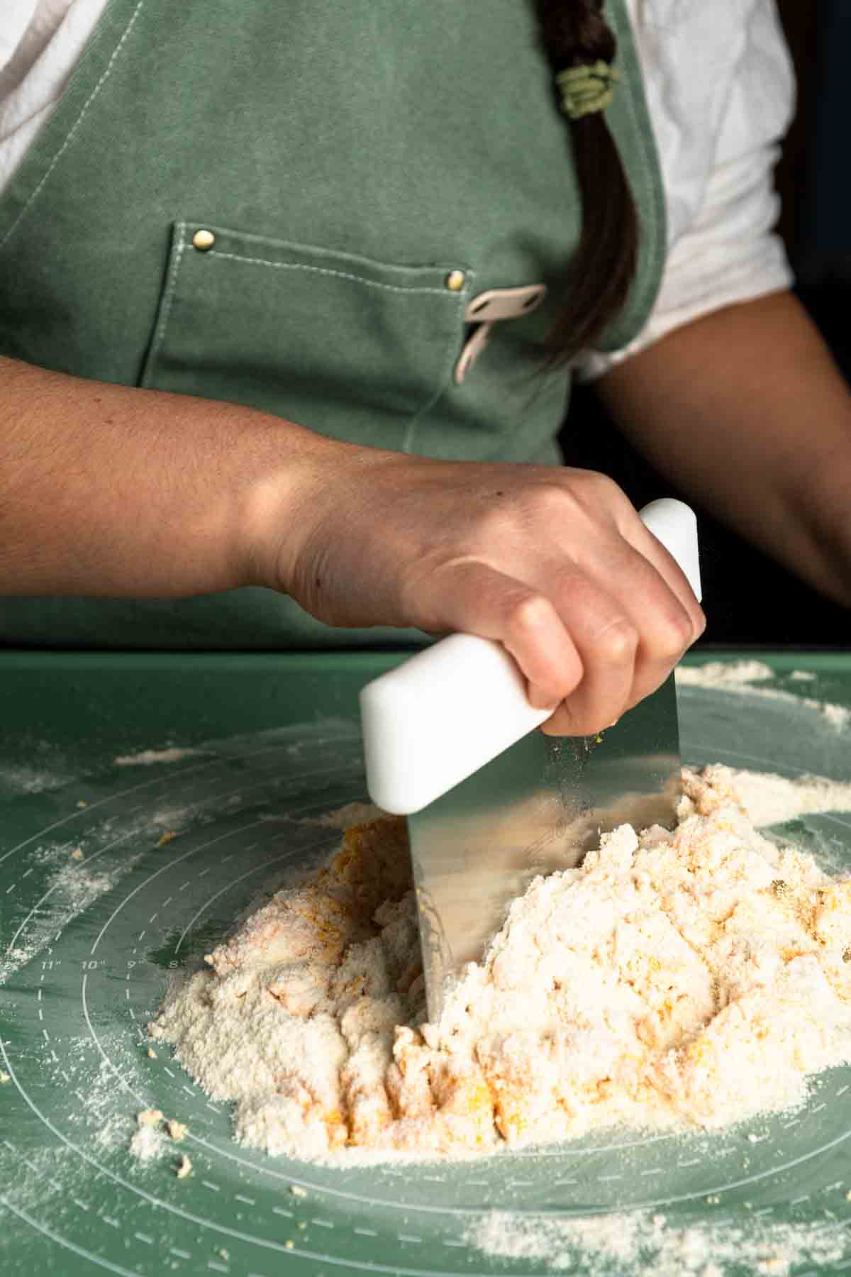 Using a bench scraper to pull the shaggy pasta dough together. 