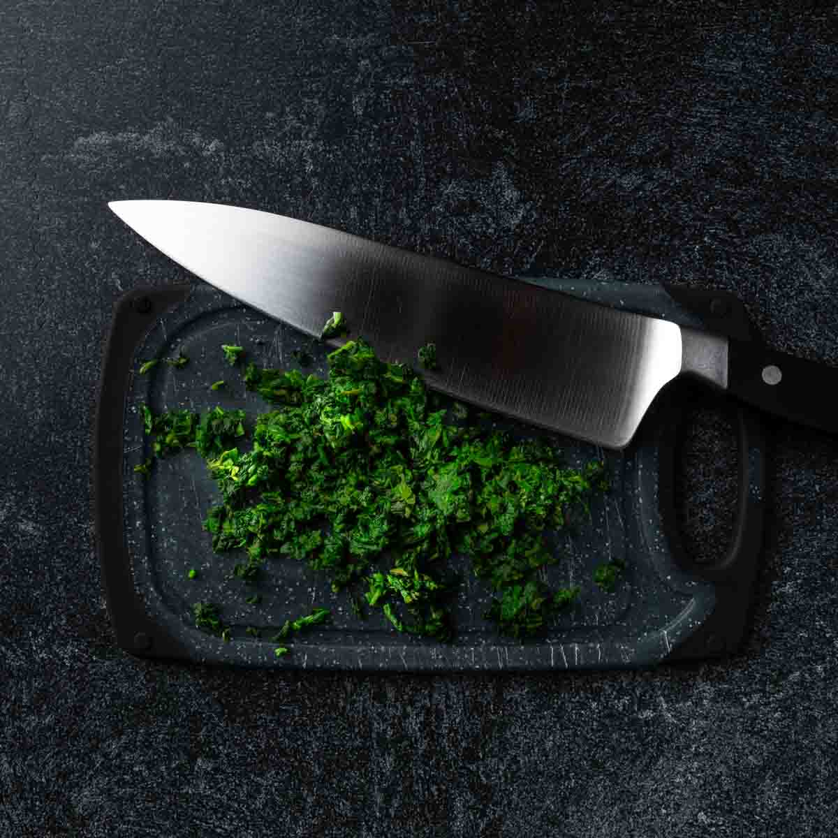 Finely chopped spinach on a cutting board with a chefs knife. 