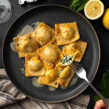 A plate of spinach ricotta ravioli in butter sauce with one half of a ravioli on a fork.