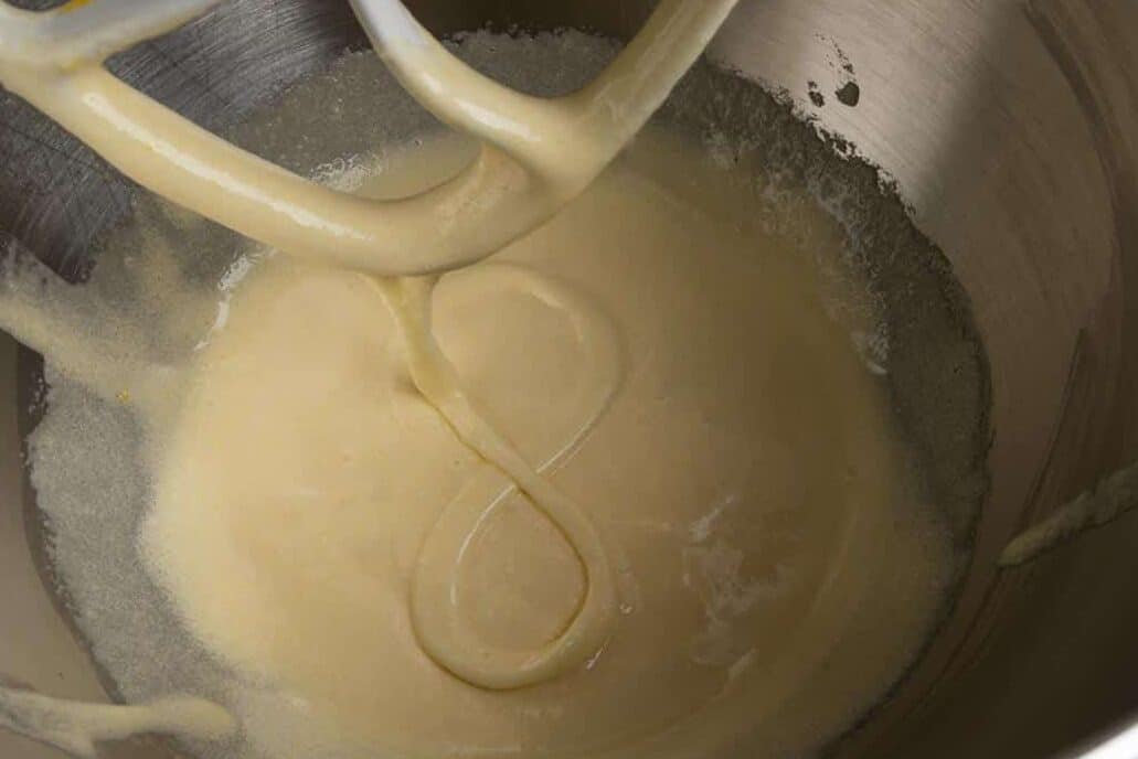 A mixture of whipped eggs and sugar falling from a mixing paddle in a figure eight.