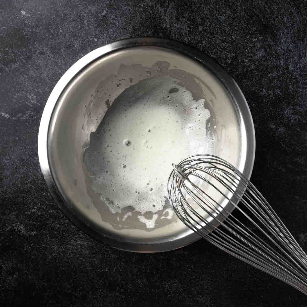 A bowl whisked with a frothy whisked egg white.