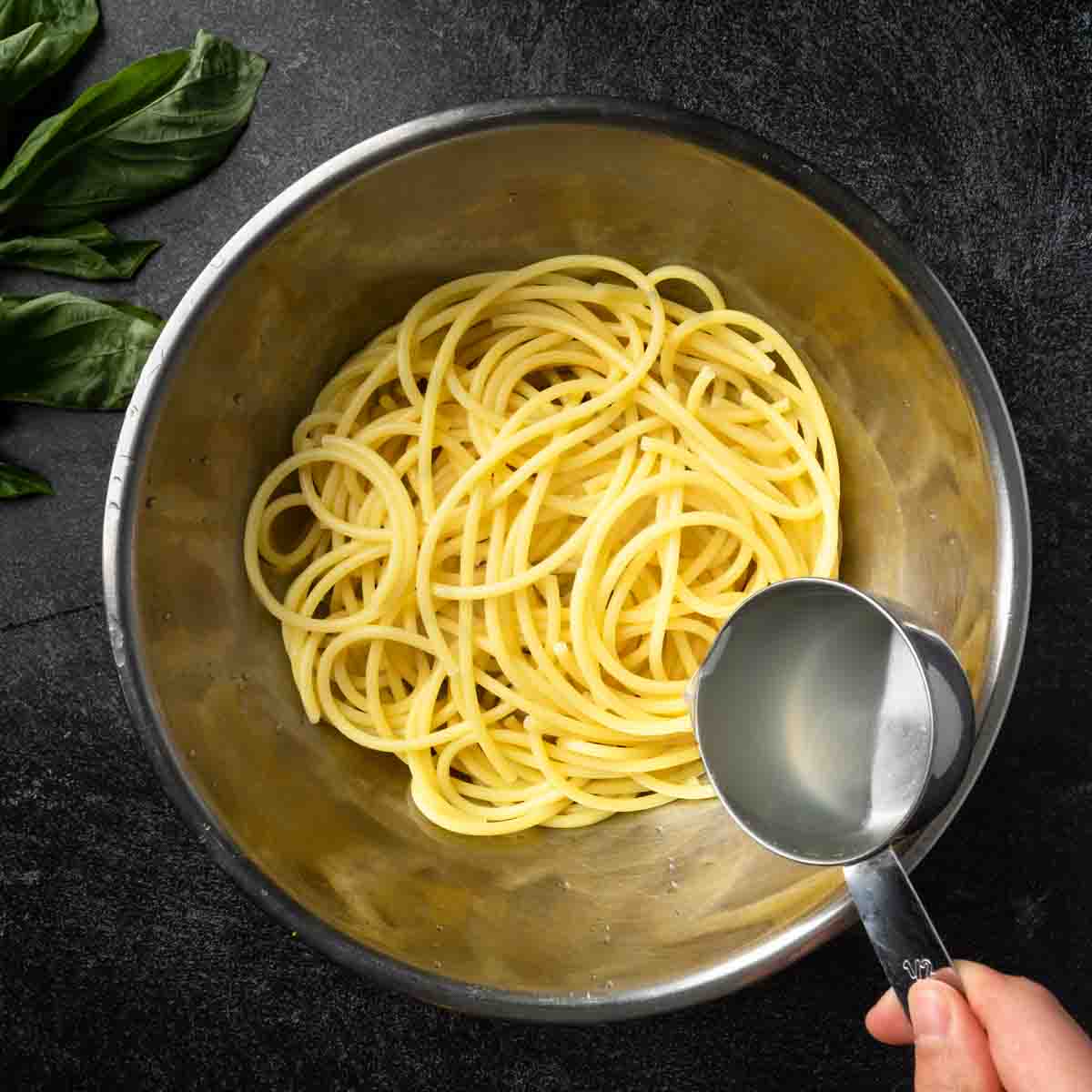 Pouring pasta water over a big bowl of spaghetti.