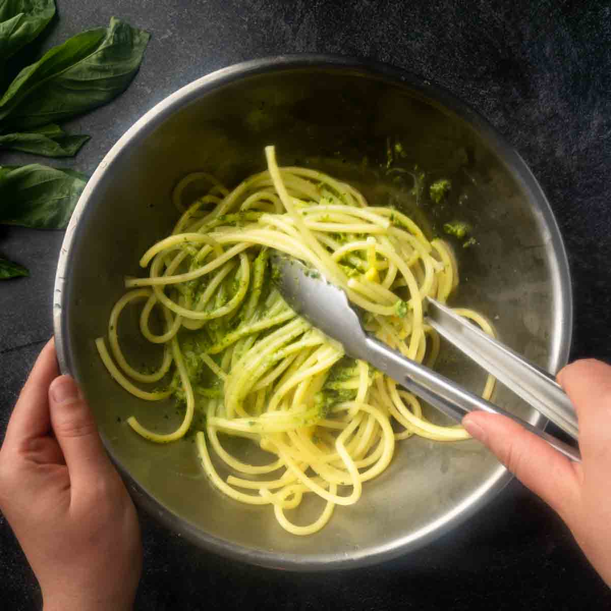Tossing the spaghetti in pesto sauce with tongs.