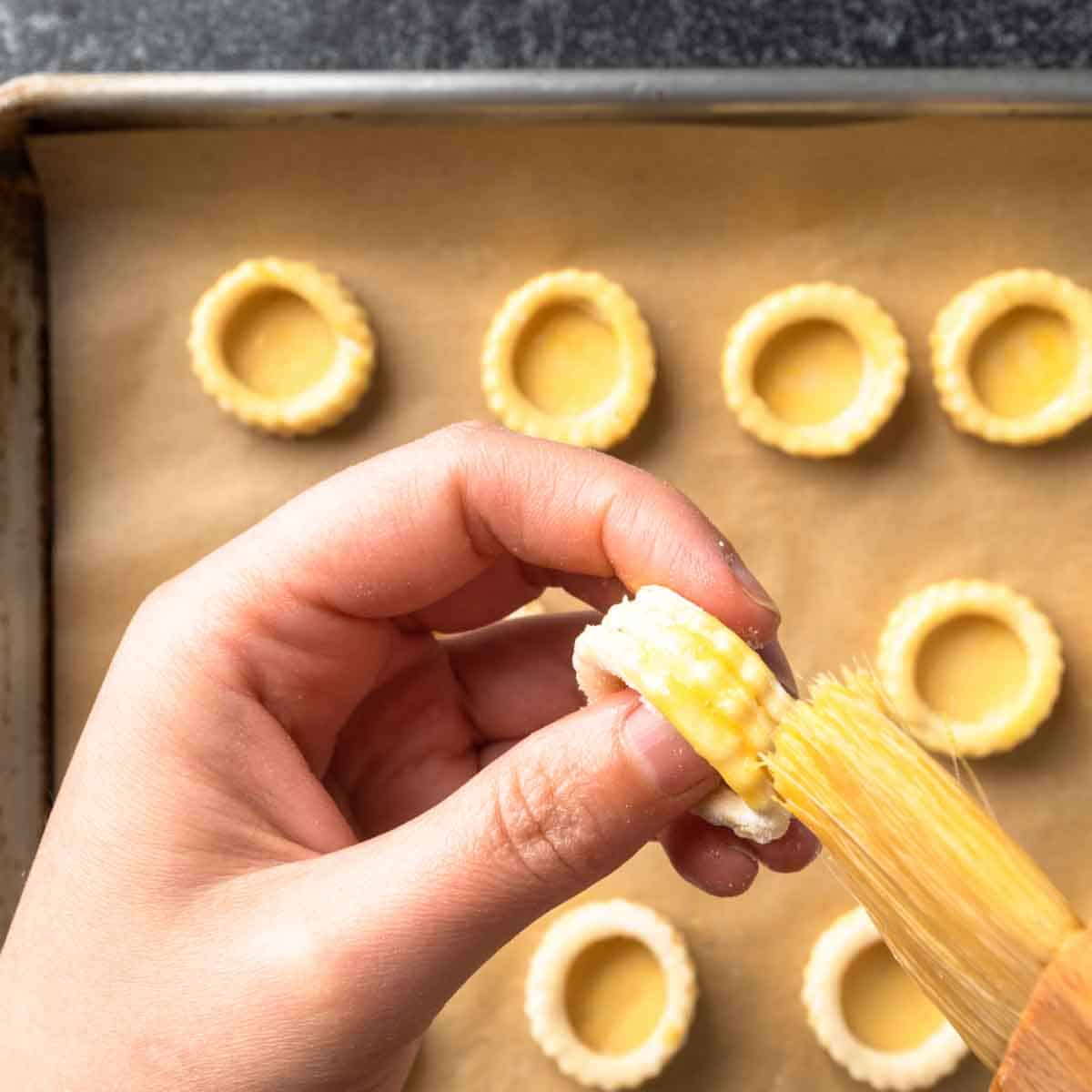 Using a pastry brush to glaze the edges of chilled, raw vol-au-vent pastries.