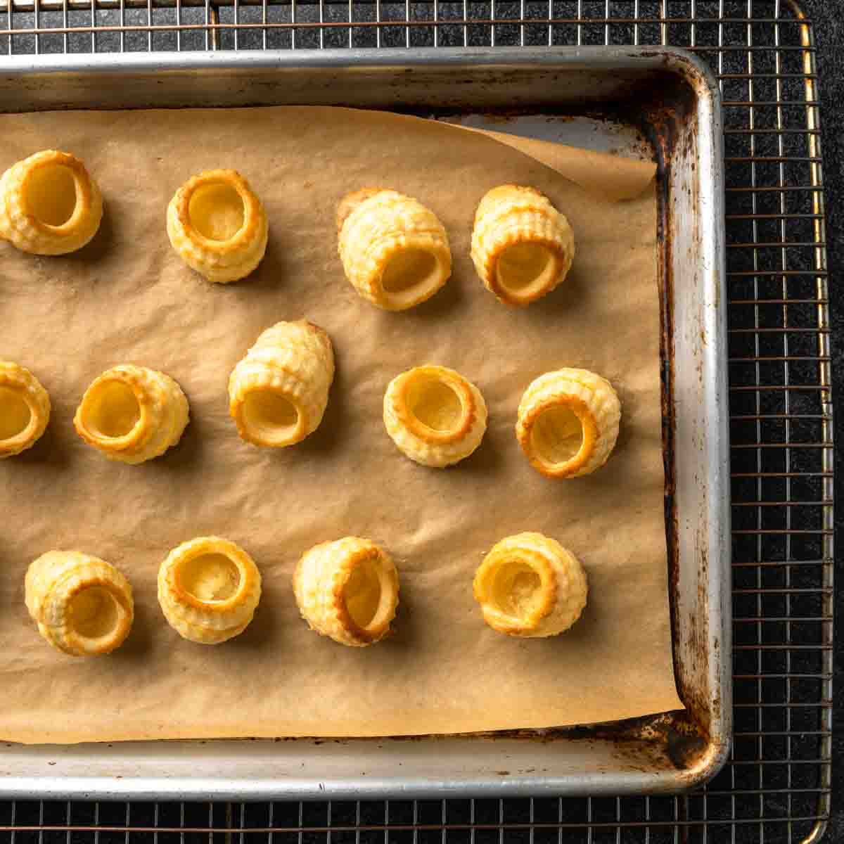 Rows of bite-sized puff pastry cups on a parchment lined baking sheet. 