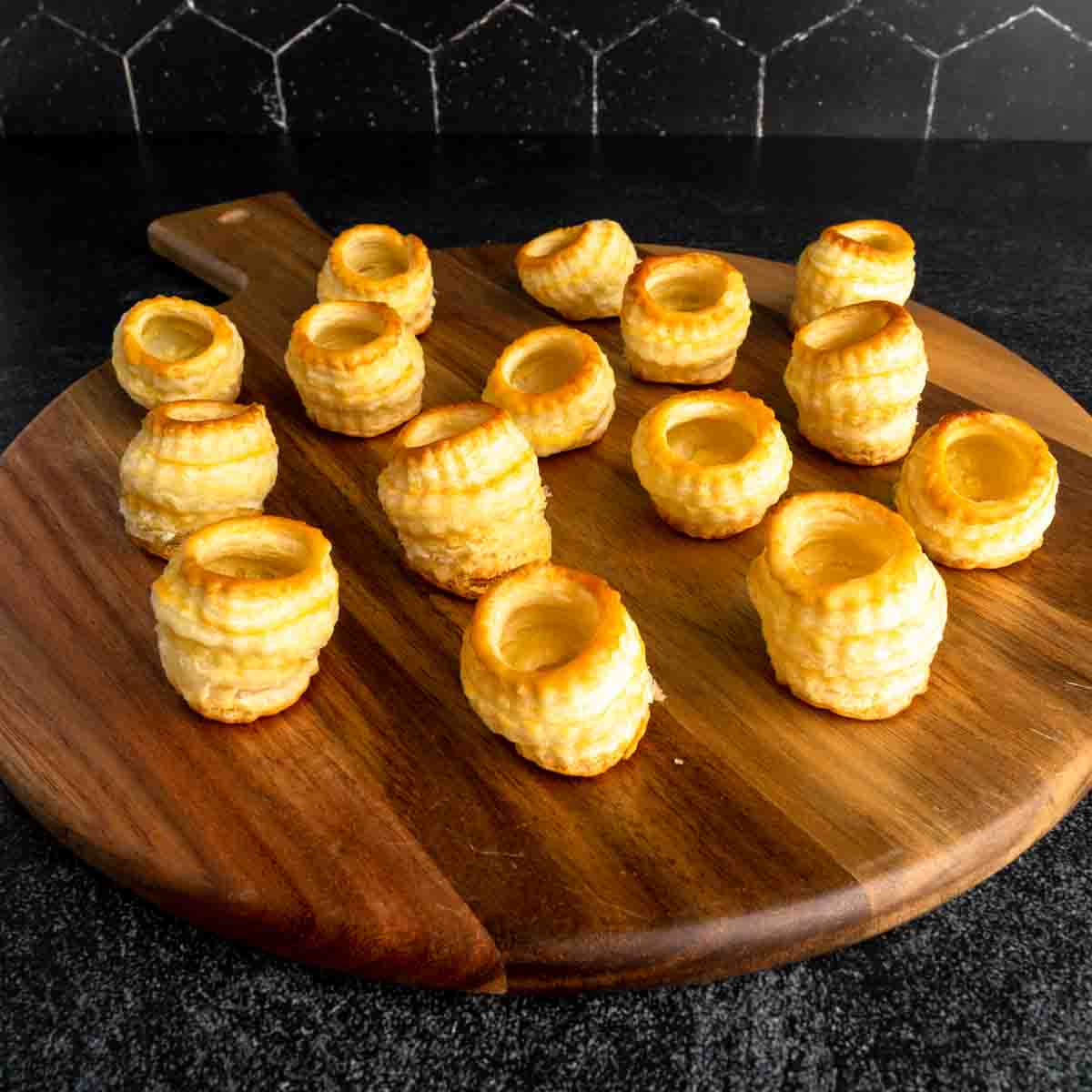A platter of miniature vol au vent pastries on a wooden tray.