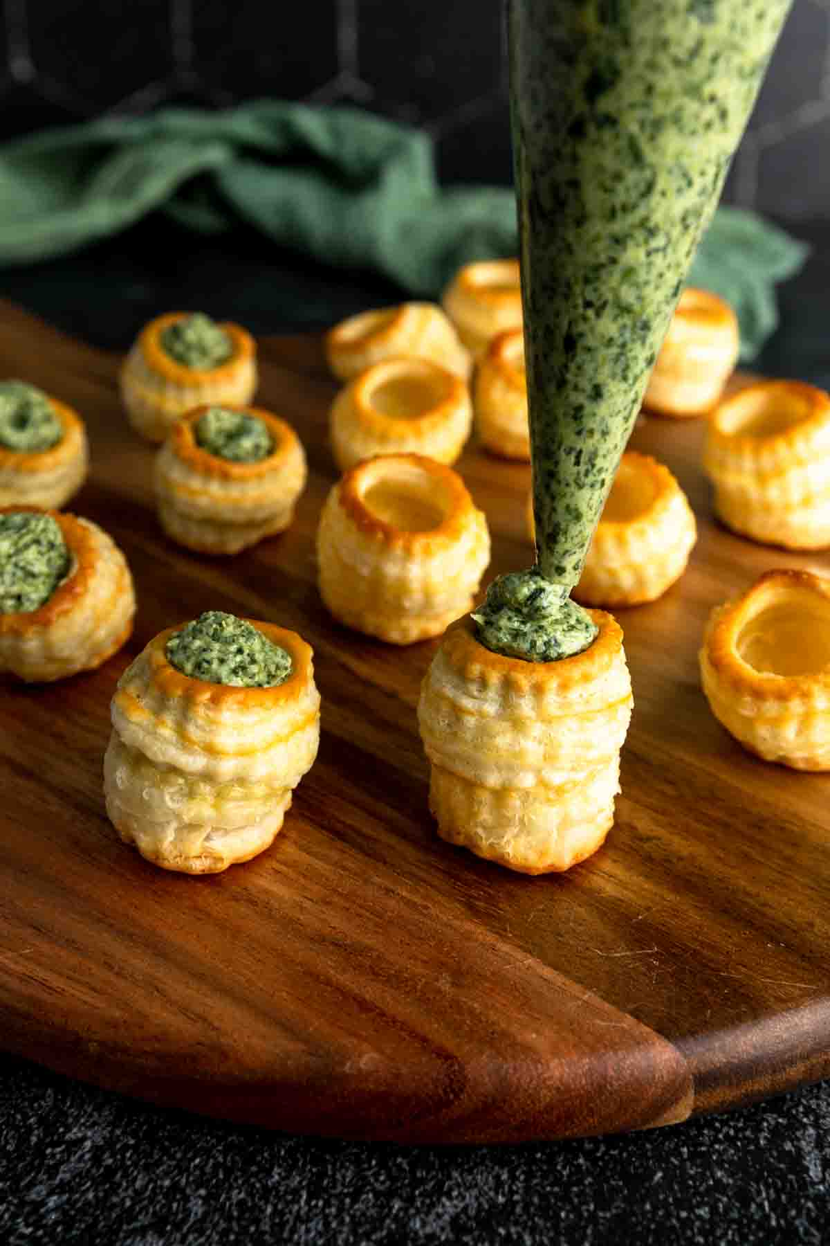 A piping bag filling a miniature puff pastry cup with spinach and artichoke dip. 