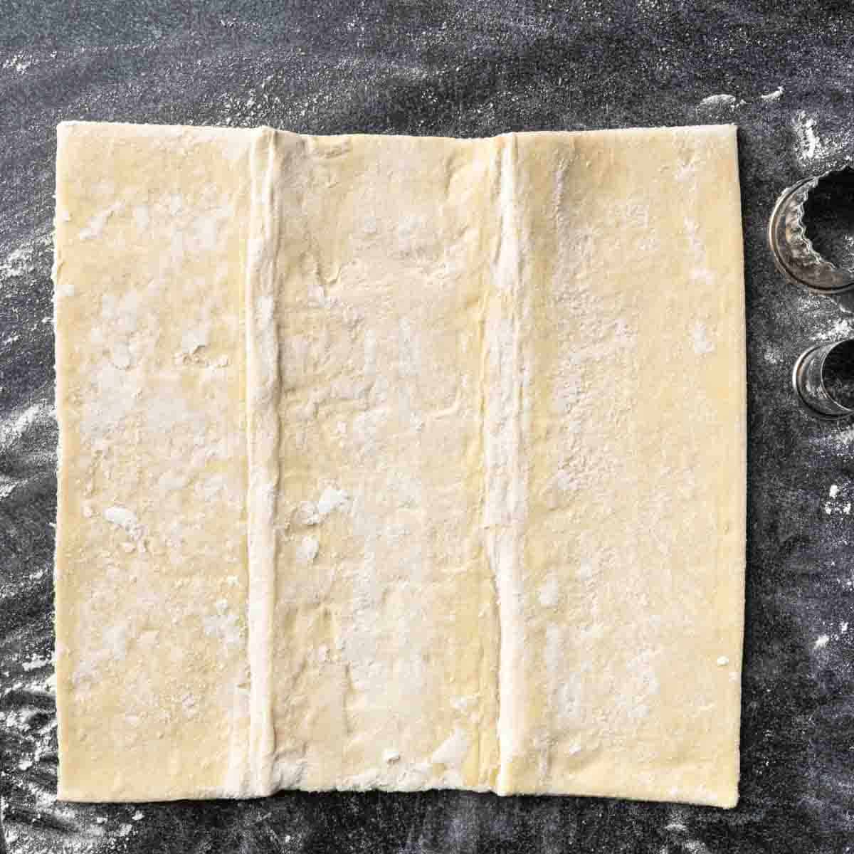 A sheet of unfolded puff pastry dough on a lightly floured counter top.