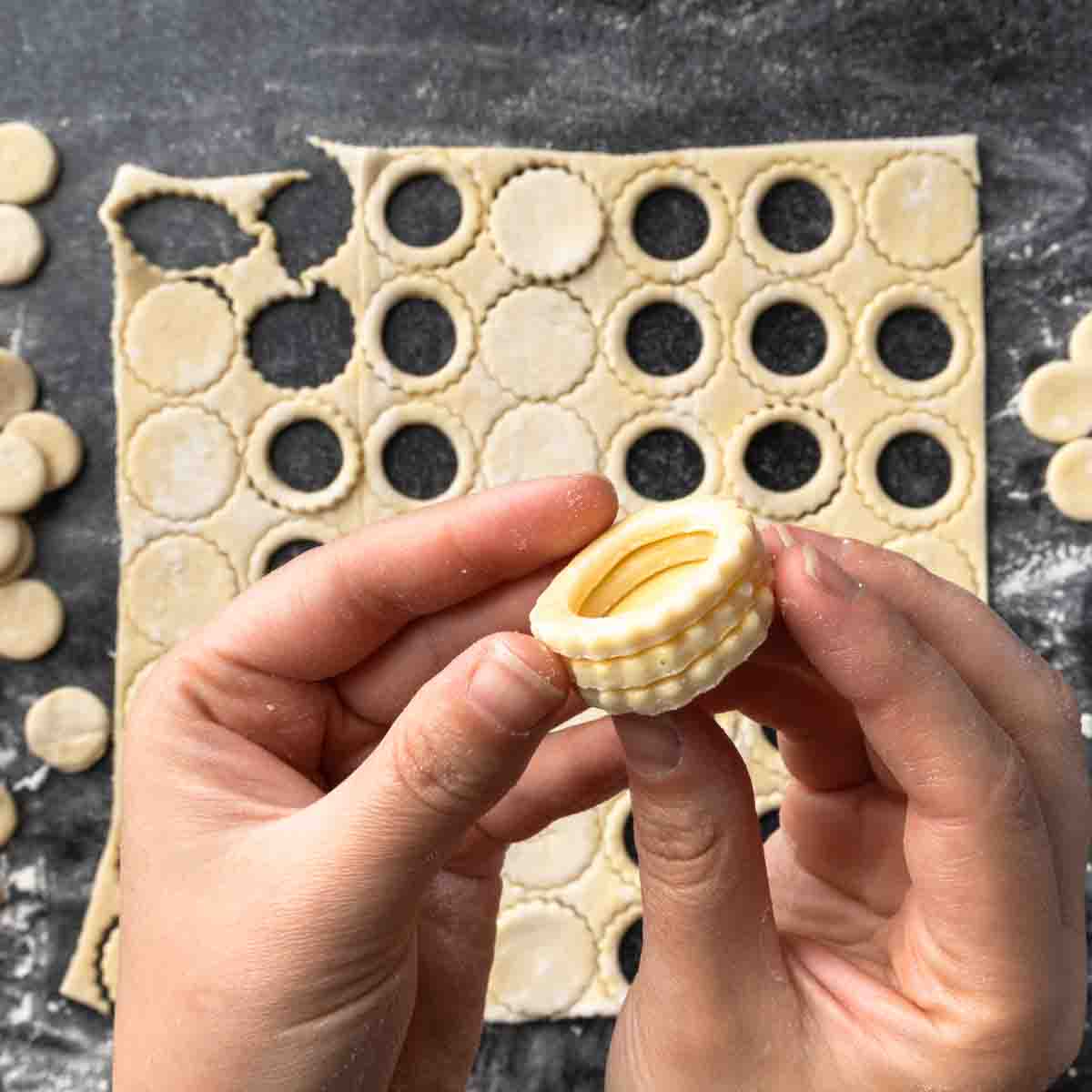 A hand holding a mini puff pastry cup made from two small rings of pastry stacked on a circle. 