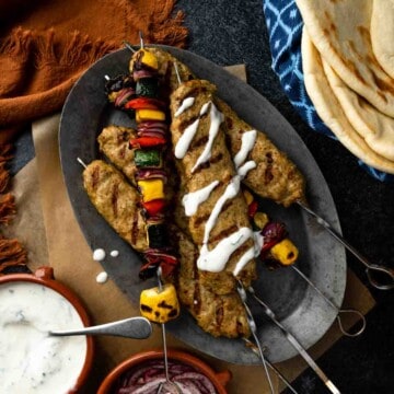 A platter of grilled chicken kofta shish kebabs with grilled vegetables and a drizzle of yogurt sauce.
