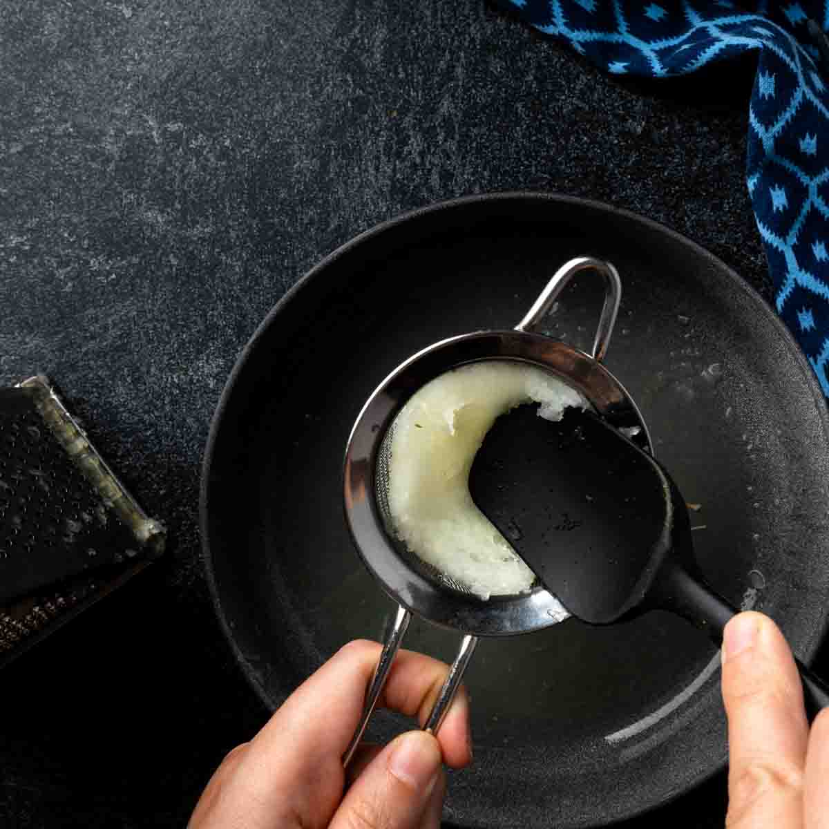 Straining the grated onion of excess juices through a fine mesh strainer.