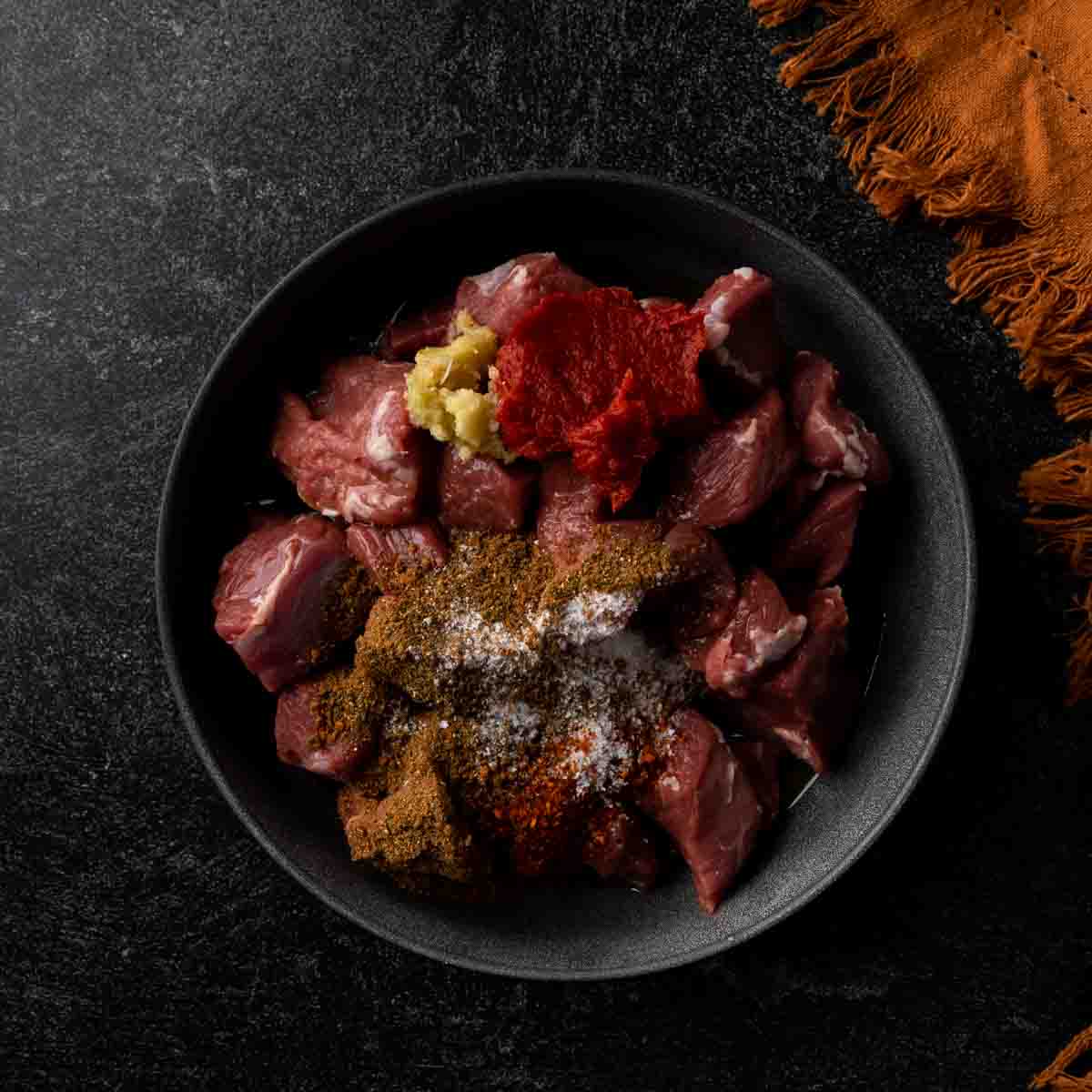 A bowl of lamb with baharat seasoning and other marinade ingredients. 