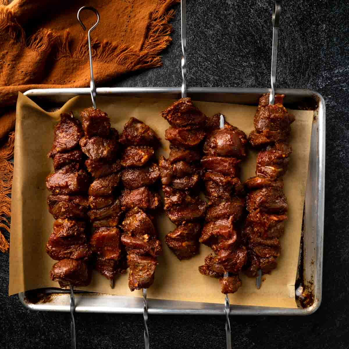 Raw marinated lamb cubes on metal skewers.