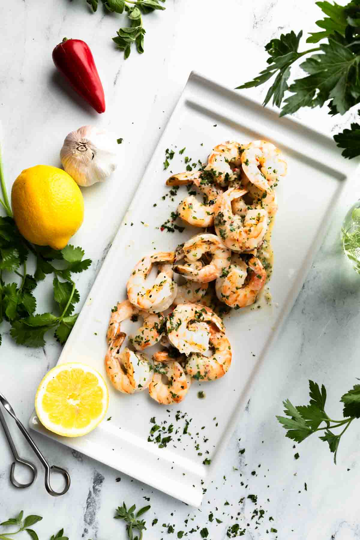 A platter of grilled chimichurri shrimp surrounded by herbs and chimichurri ingredients. 