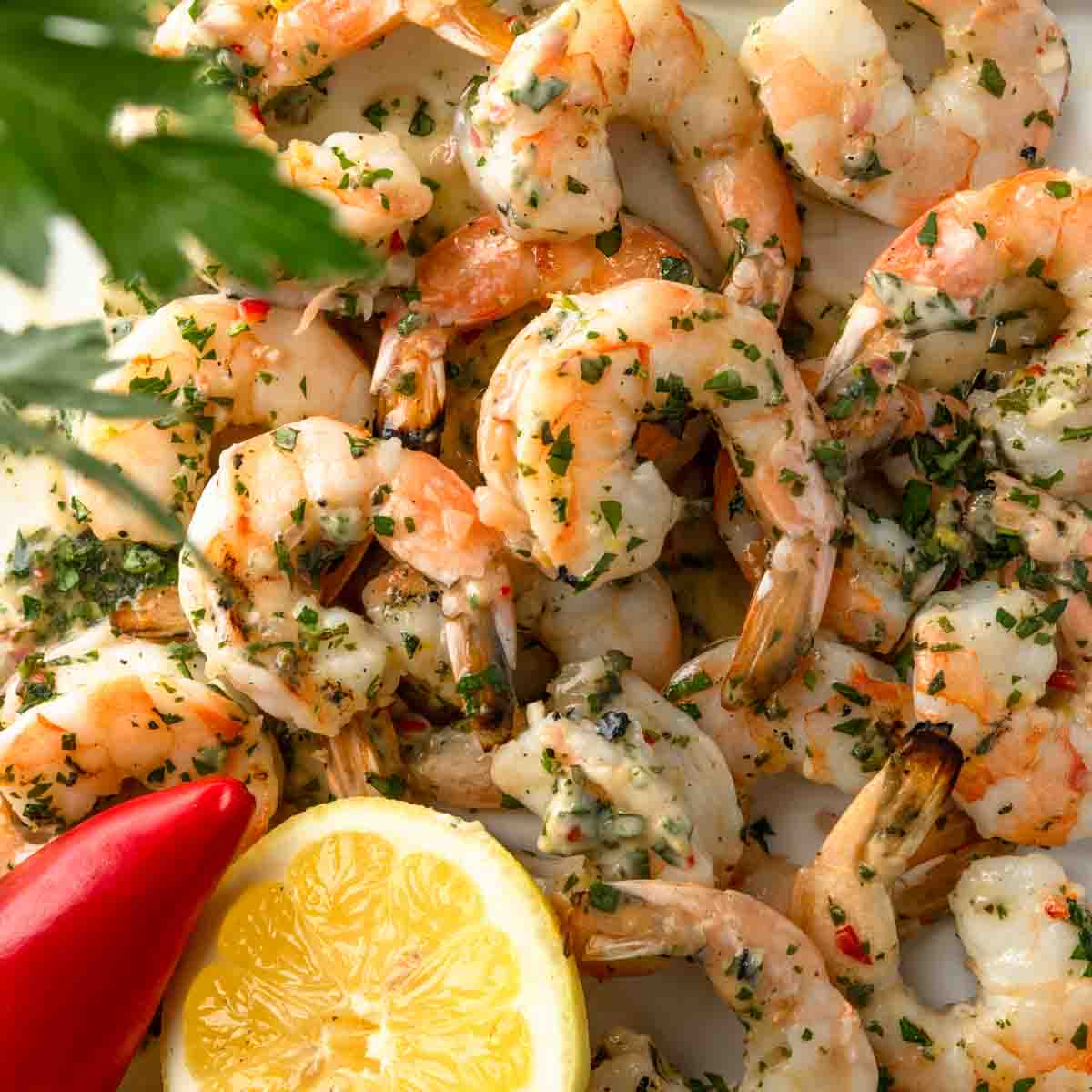 A close up picture of grilled shrimp tossed in chimichurri butter with a halved lemon. 