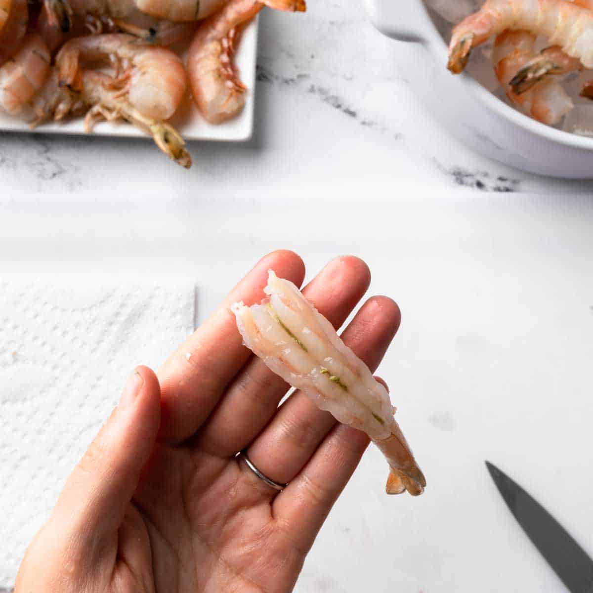A hand holding a fresh shrimp that has been split to reveal the vein.