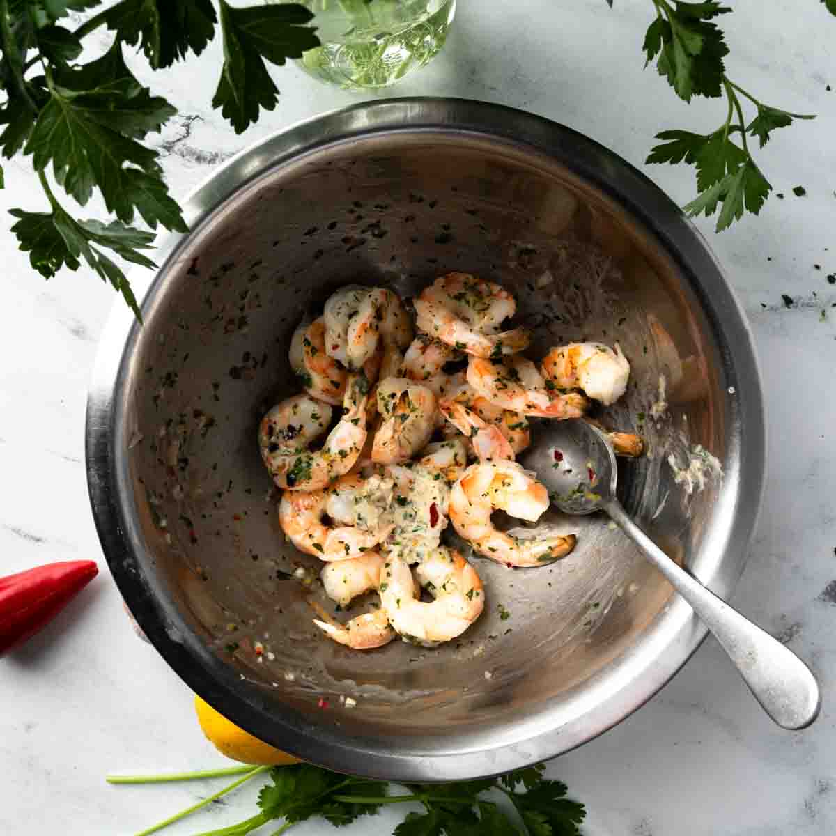 Grilled shrimp being tossed in a big bowl with chimichurri butter.