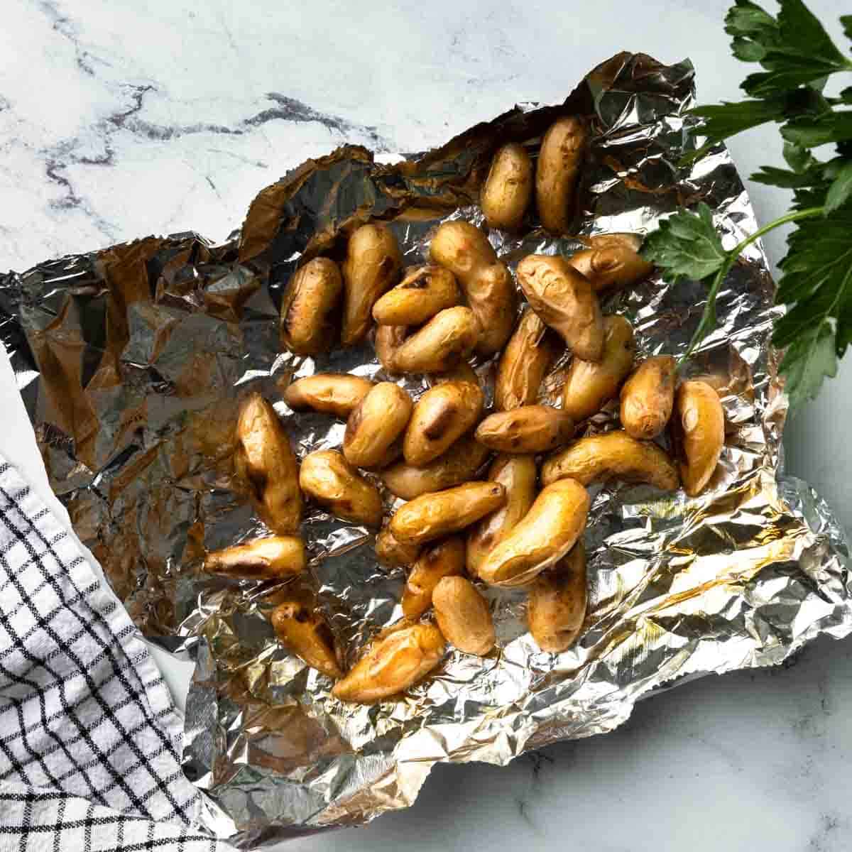 A pile of grilled fingerling potatoes on a sheet of aluminum foil. 