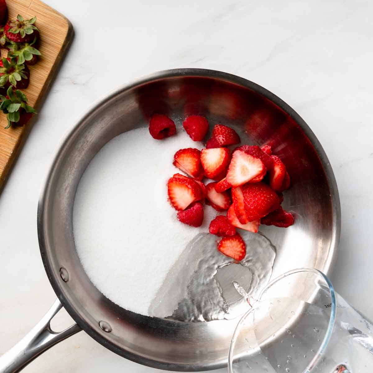 A saucepan with strawberries, raspberries, sugar and water. 