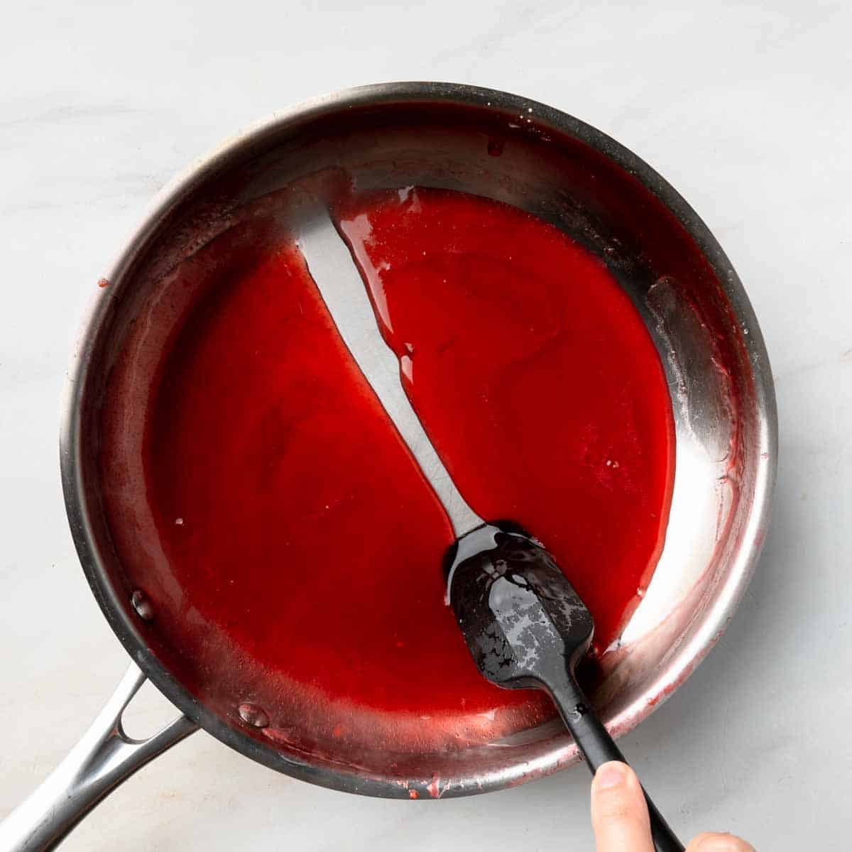 A spatula drawing a line through a pan of thickened berry syrup. 