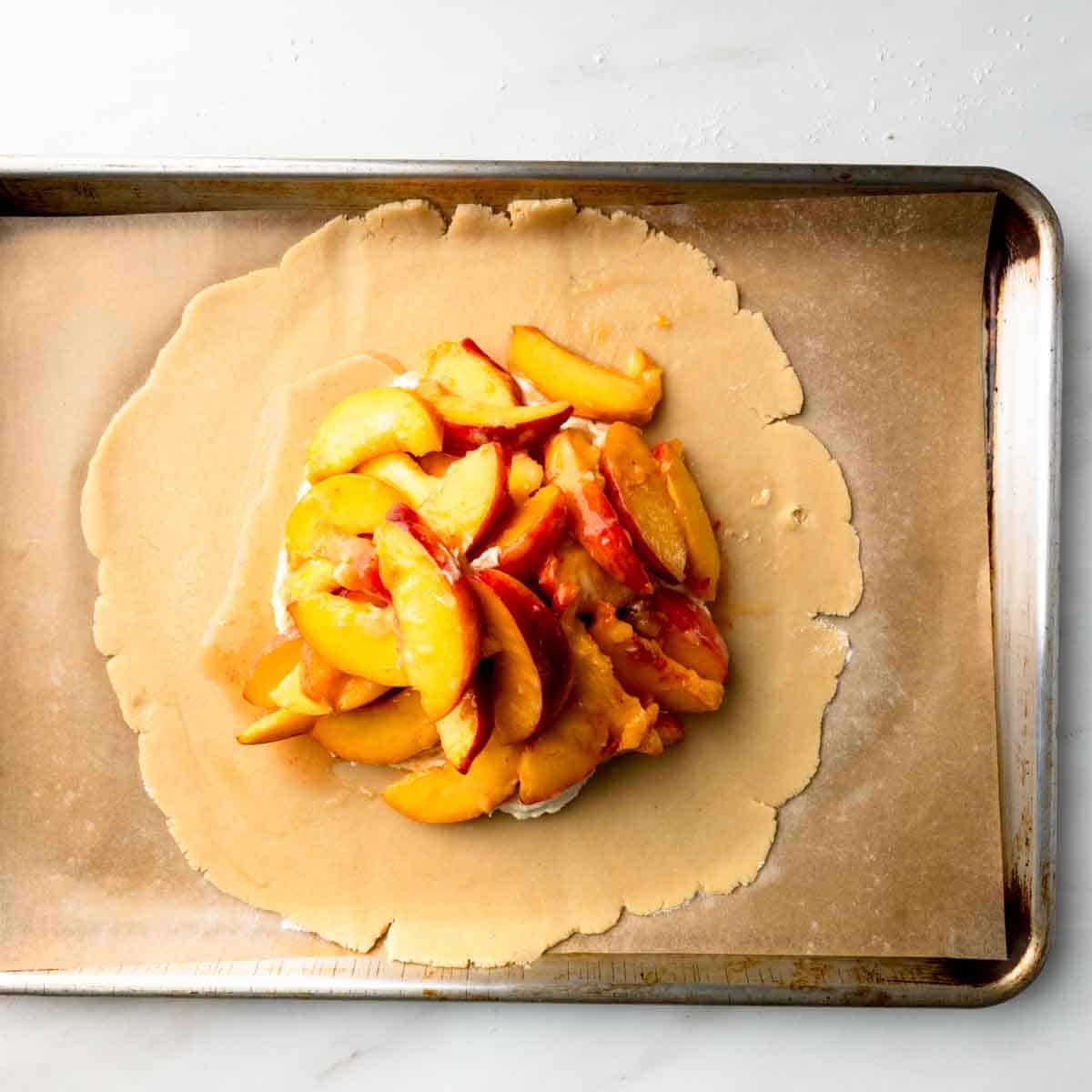 Raw peach slices piled on the circle of Italian pastry dough.