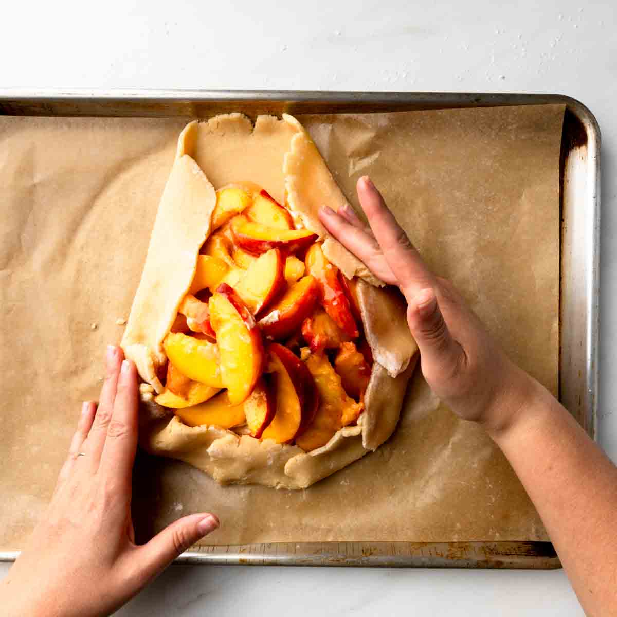 Pleating pasta frolla pastry dough around the edges of the peach crostata filling. 