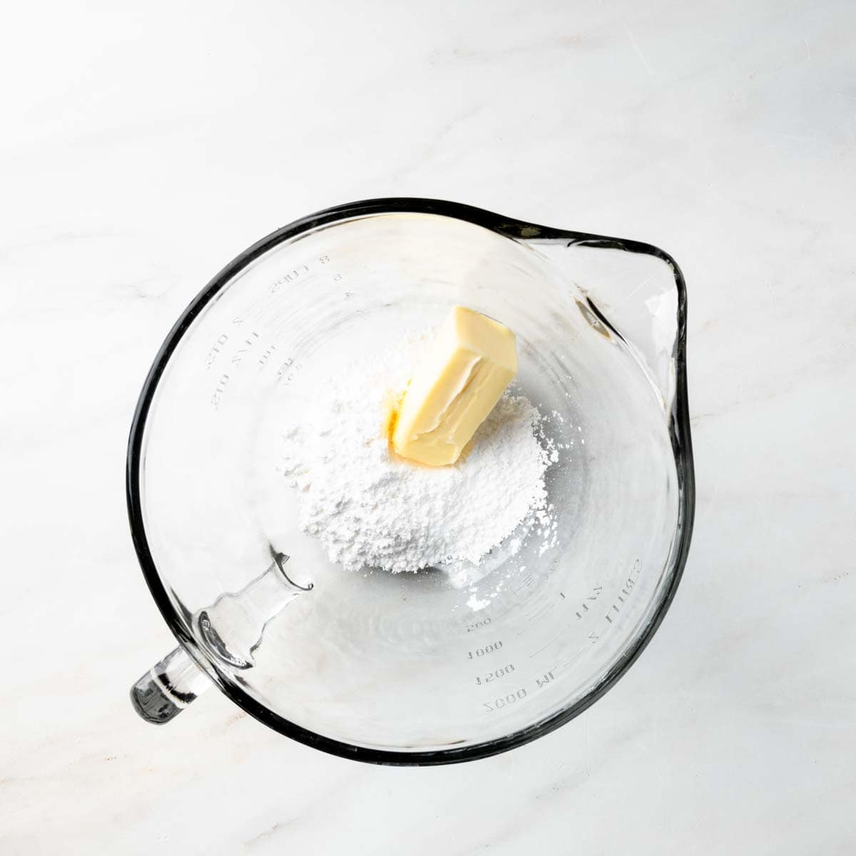 A mixing bowl with powdered sugar and a stick of butter.