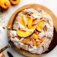 A big slice being lifted from a peach frangipane tart dusted in powdered sugar.