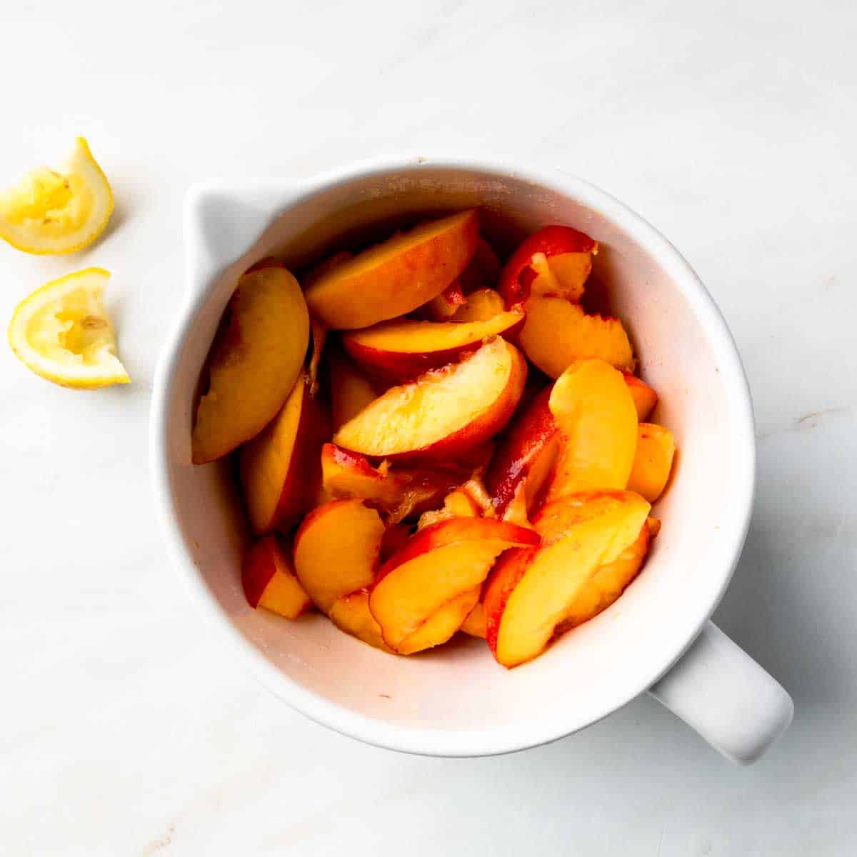 A bowl of sugared peach slices next to squeezed lemon wedges. 