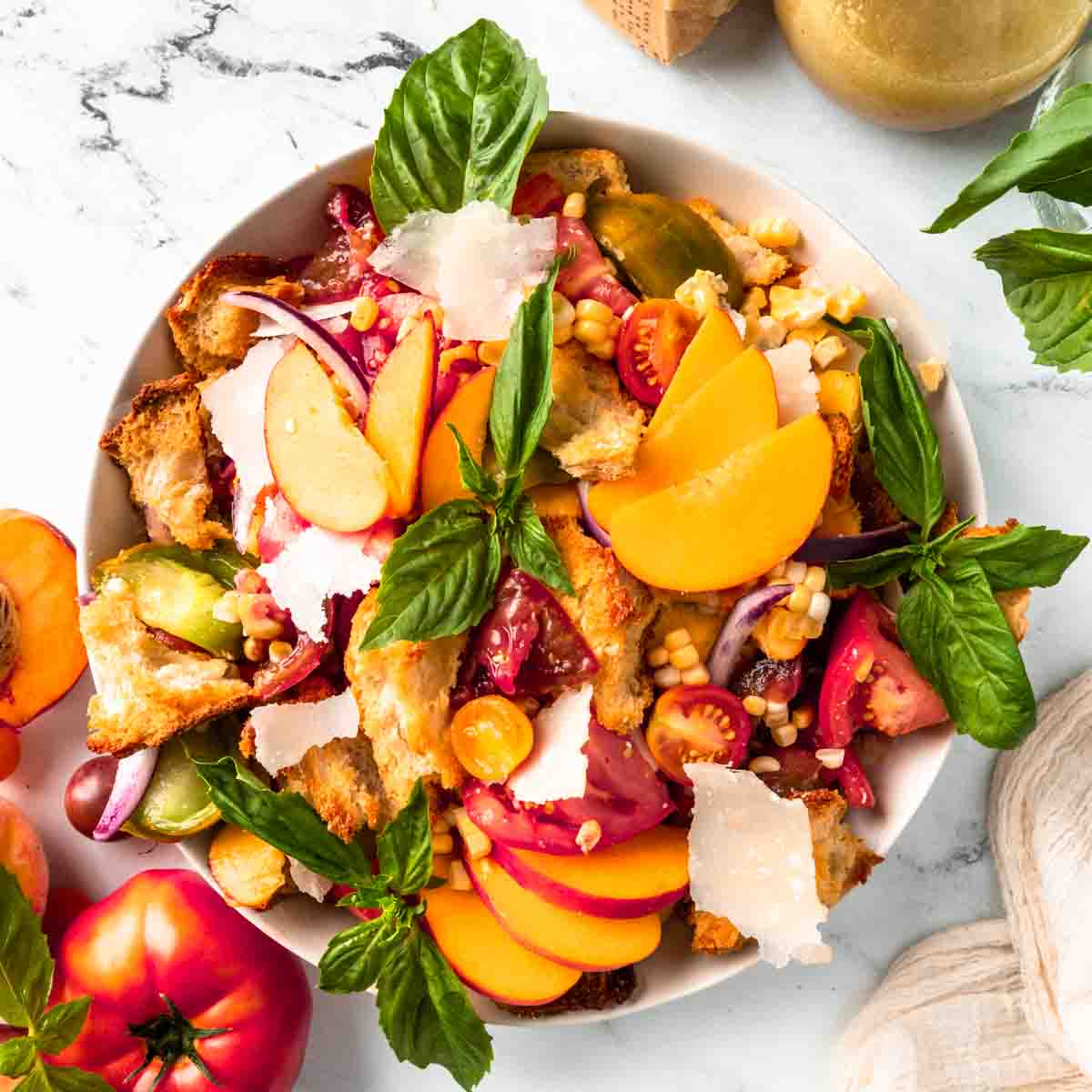 A white bowl filled with peach panzanella salad with tomatoes and basil. 