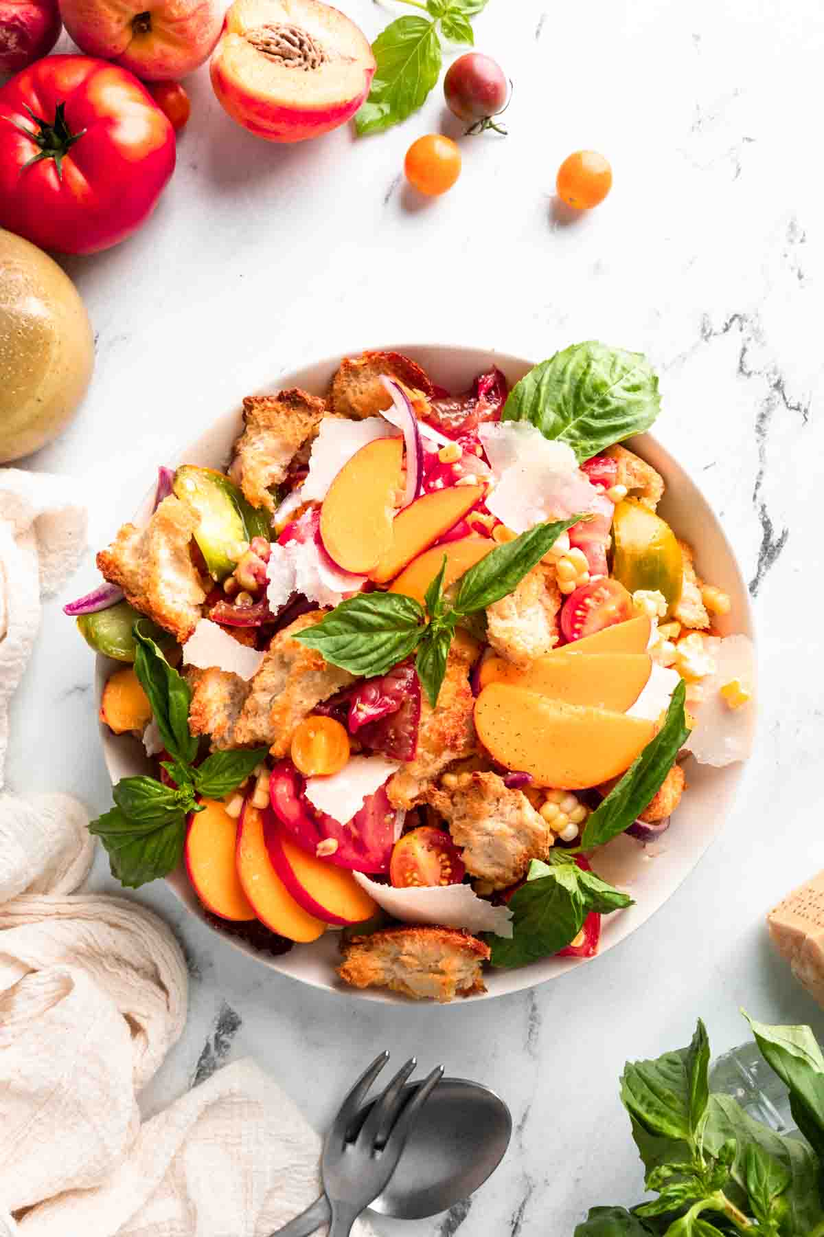 A flatly photo of peach panzanella salad surrounded by peaches and tomatoes. 