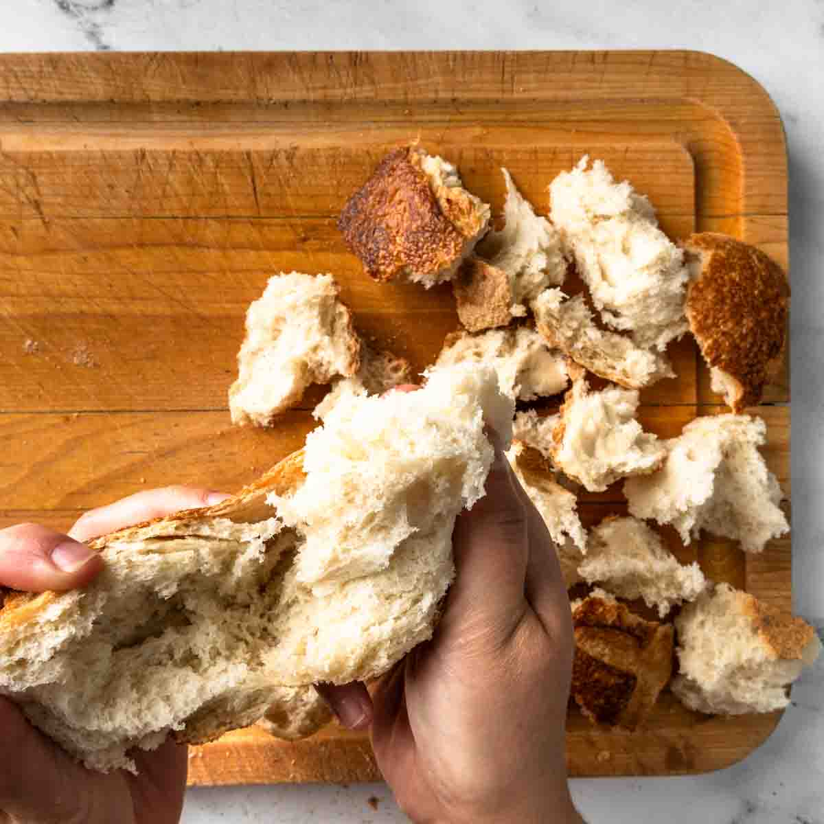 Hand tearing a loaf of sourdough bread into chunks for croutons. 