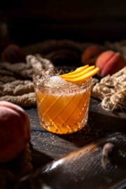 A glass of peach pie punch garnished with a fan of fresh peach slices.