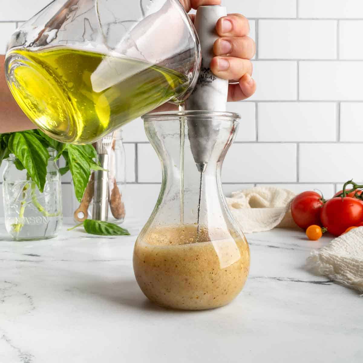 Whisking and emulsifying oil into the dressing.